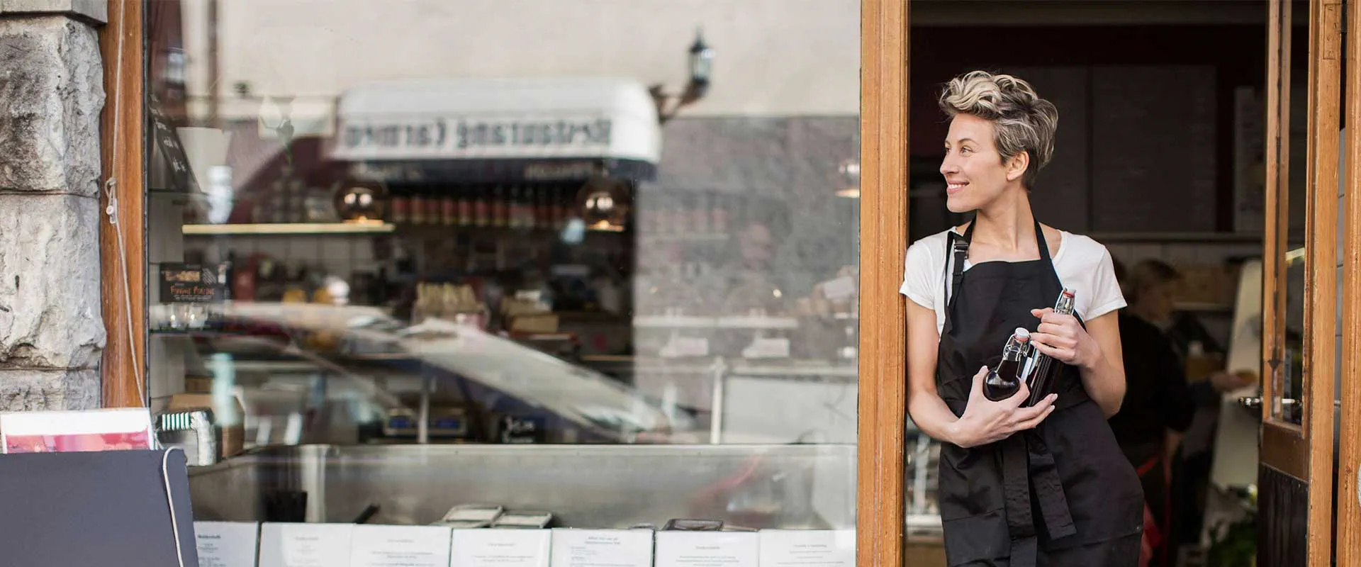 Hospitality worker standing outside a café holding a tray and smiling Hospitality worker standing outside a café holding a tray and smiling