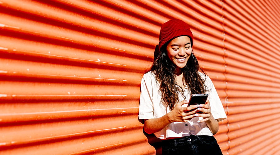 Person using smartphone against red wall outdoors