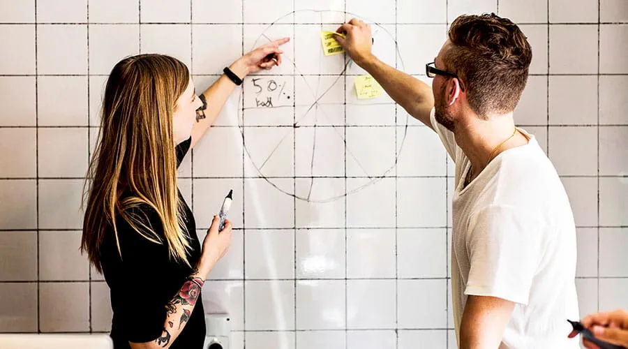 Two colleagues writing on board during brainstorming Two colleagues writing on board during brainstorming