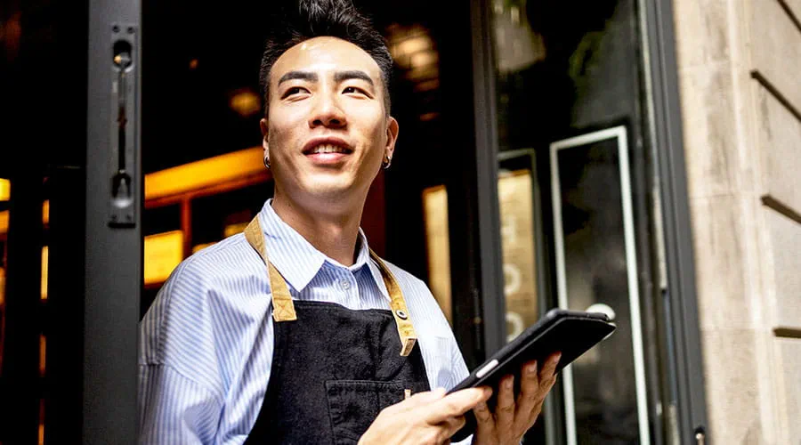 Camarero sosteniendo una tableta y sonriendo en un entorno de restaurante Camarero sosteniendo una tableta y sonriendo en un entorno de restaurante