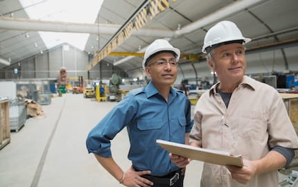 Deux salariés seniors, équipés de casques blancs, travaillent dans un atelier professionnel. Deux salariés seniors, équipés de casques blancs, travaillent dans un atelier professionnel.