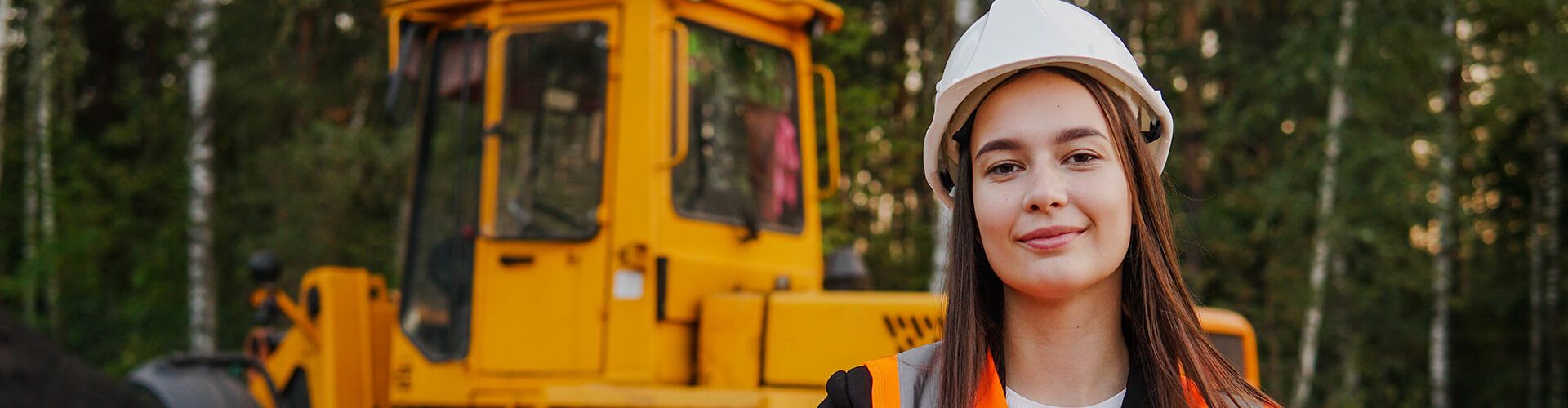 Une femme avec un casque de chantier devant un engin de chantier