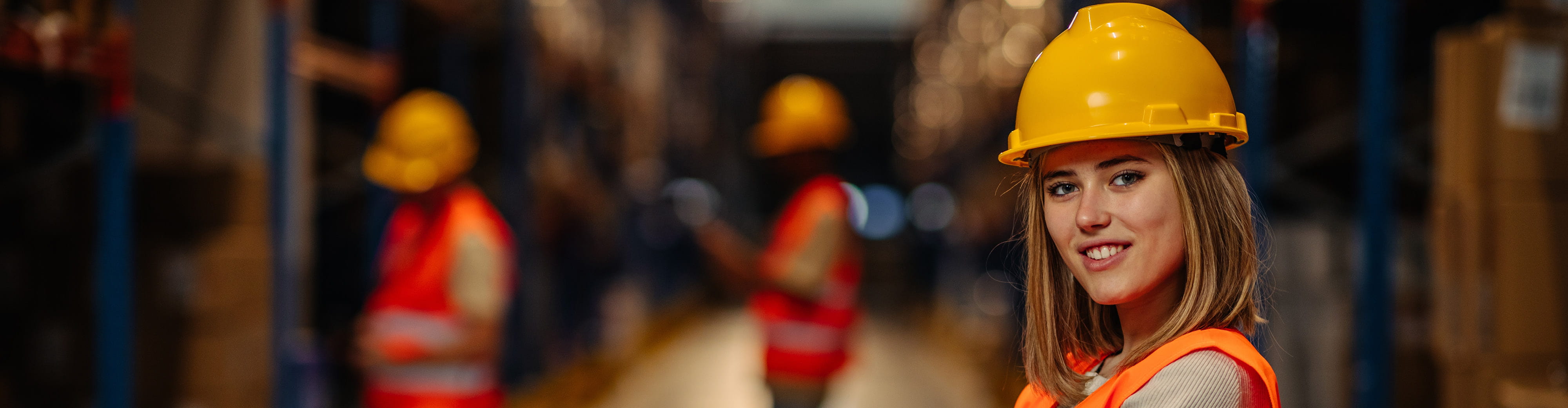 Une femme blonde aux cheveux courts avec un casque sur la tête travaille dans un entrepôt.
