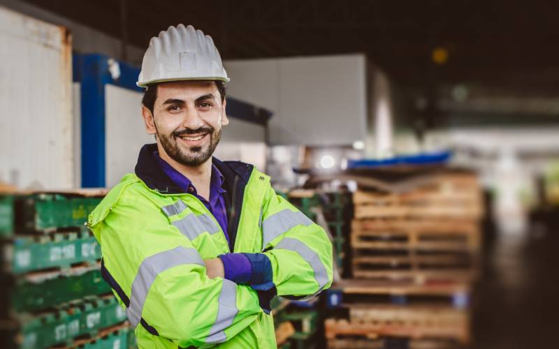 Un jeune homme travaillant dans la logistique sourit avec son casque et son gilet fluo