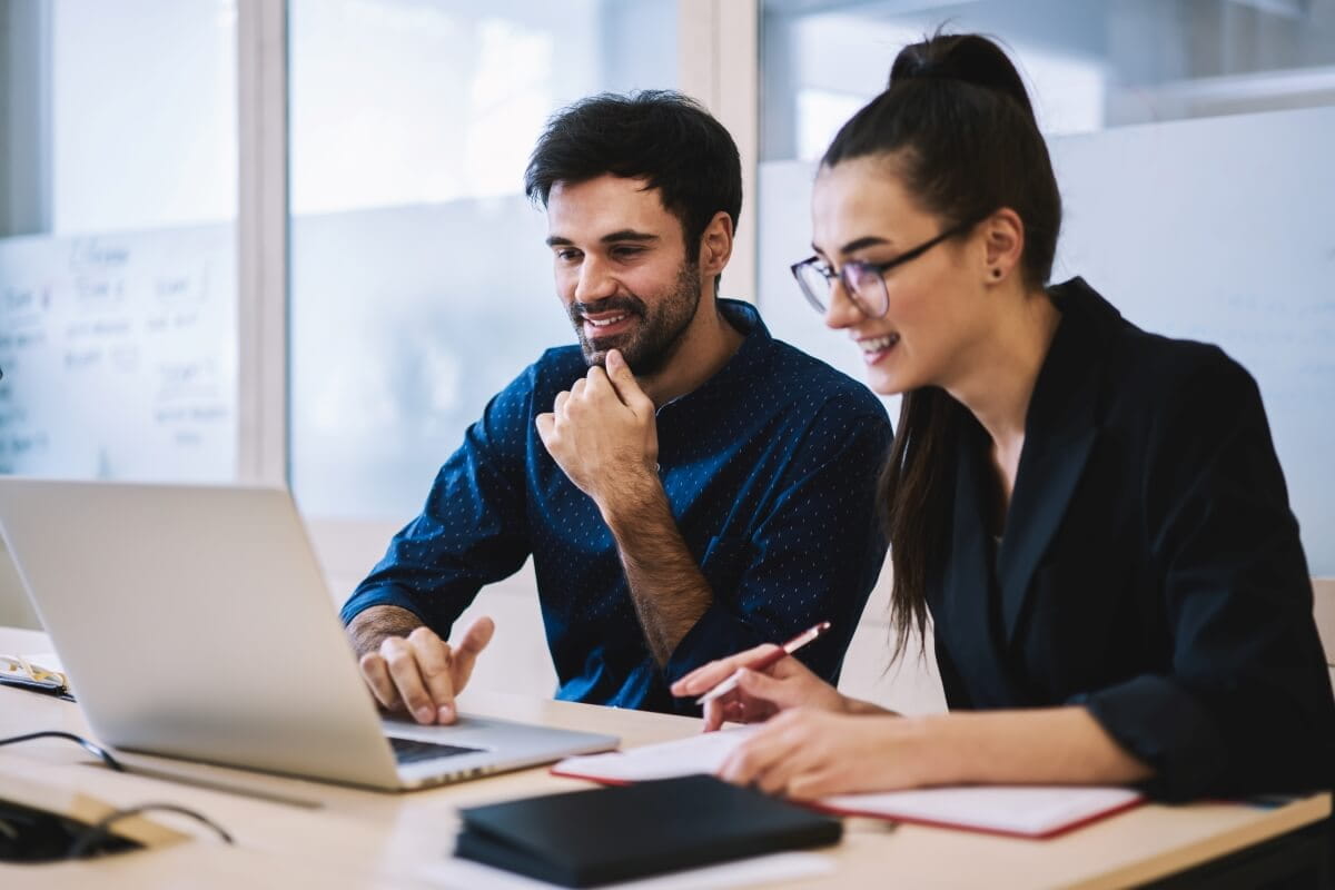 Deux jeunes professionnels souriants travaillent ensemble sur un ordinateur portable à un bureau