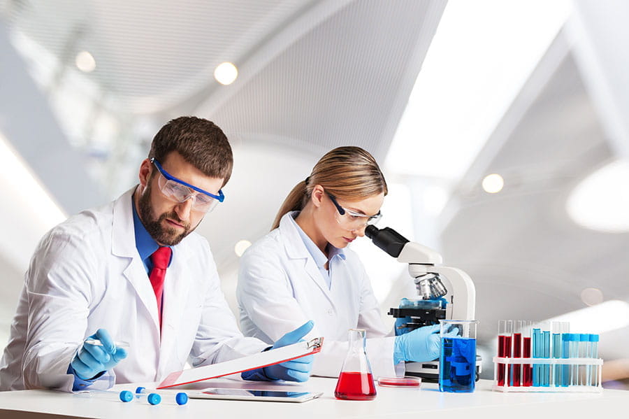 Deux scientifiques en blouses blanches et lunettes de protection travaillent dans un laboratoire avec un microscope et des éprouvettes