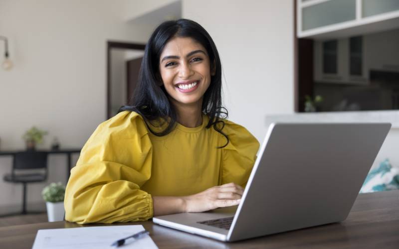 Une jeune femme souriante en chemisier jaune travaillant sur un ordinateur portable à une table