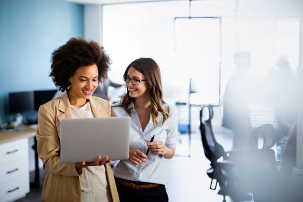 Deux jeunes femmes professionnelles souriantes regardent un ordinateur portable dans un bureau lumineux