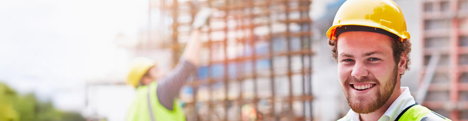 Un homme souriant avec un casque de chantier jaune sur un lieu de construction