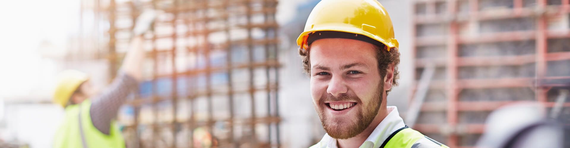 Un homme souriant avec un casque de chantier jaune sur un lieu de construction