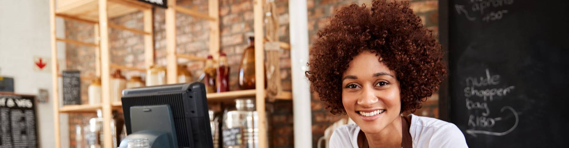 Une vendeuse souriante d'une épicerie zéro déchet derrière un comptoir en bois