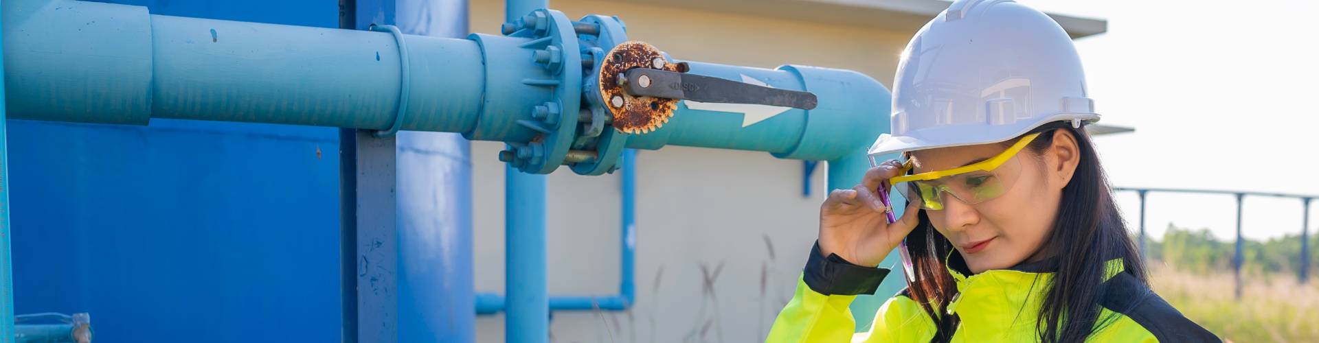 Une technicienne avec un casque blanc devant des tuyaux
