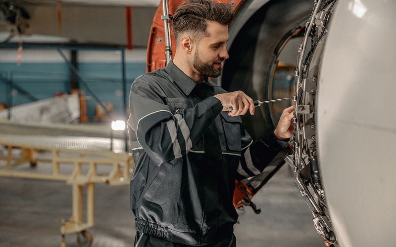Homme souriant technicien d'entretien aérien utilisant un tournevis pendant la réparation de l'avion