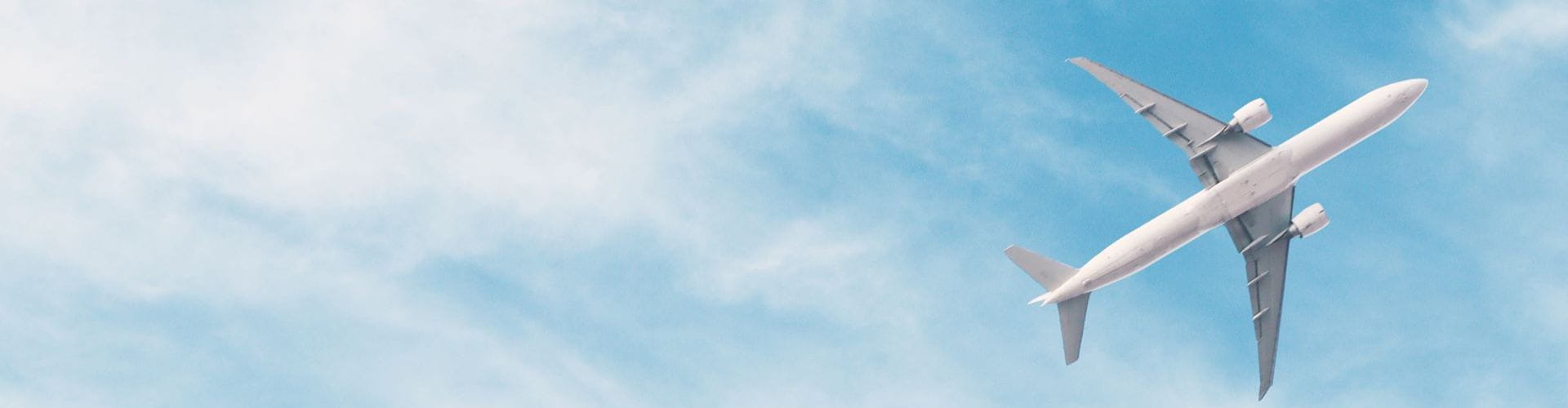 Un avion de ligne blanc vu d'en bas, volant dans un ciel bleu clair avec quelques nuages
