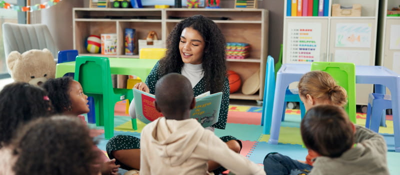 Une auxiliaire de puériculture lisant un livre à un groupe d'enfants dans une crèche 