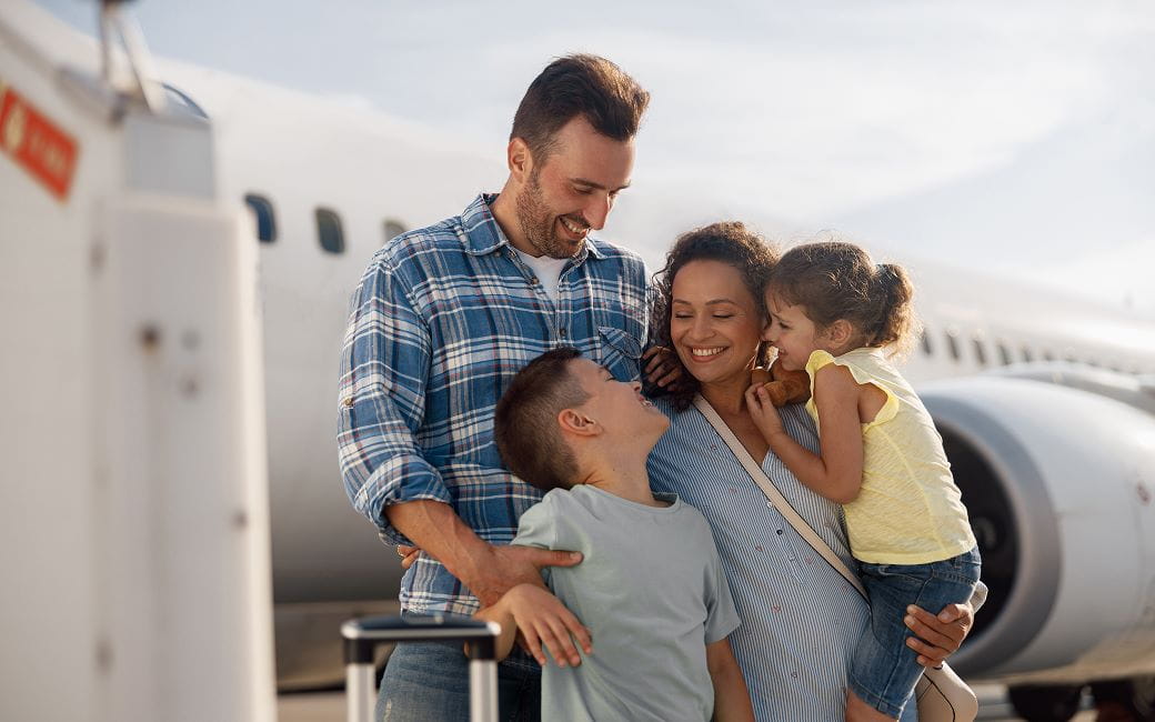  Famille de quatre personnes , excitée pendant un voyage, debout devant un grand avion à l'extérieur.
