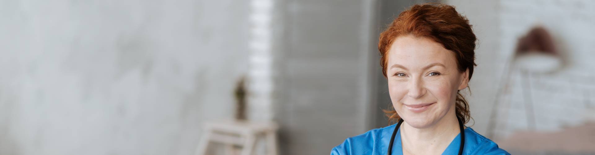 une aide-soigante avec une blouse bleu en CDI intérimaire sourit