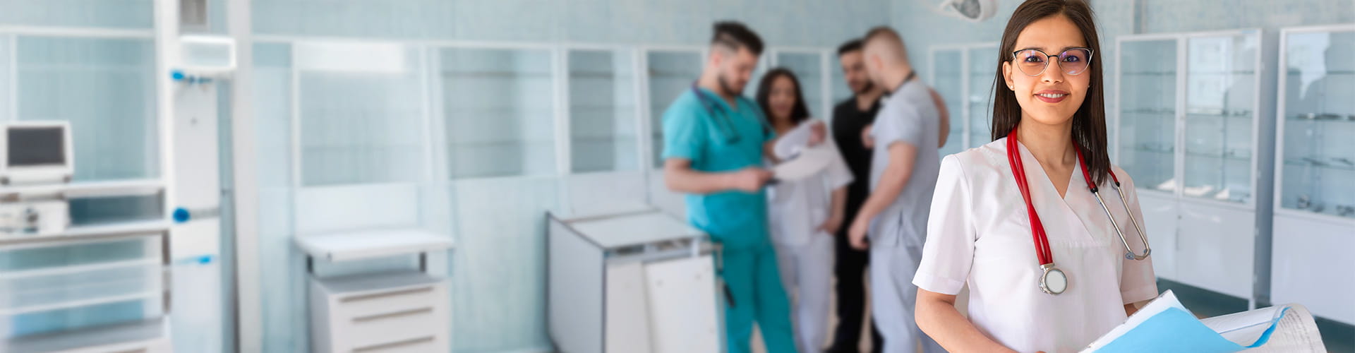 Une professionnelle de la santé souriante avec un stéthoscope et un dossier, debout dans un hôpital avec d'autres professionnels de la santé en arrière-plan