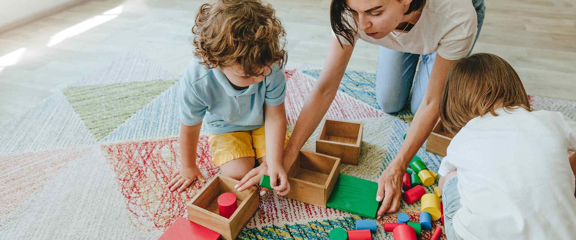 Jeune enseignante jouant dans une maternelle avec des enfants par terre avec des jouets en bois multicolore