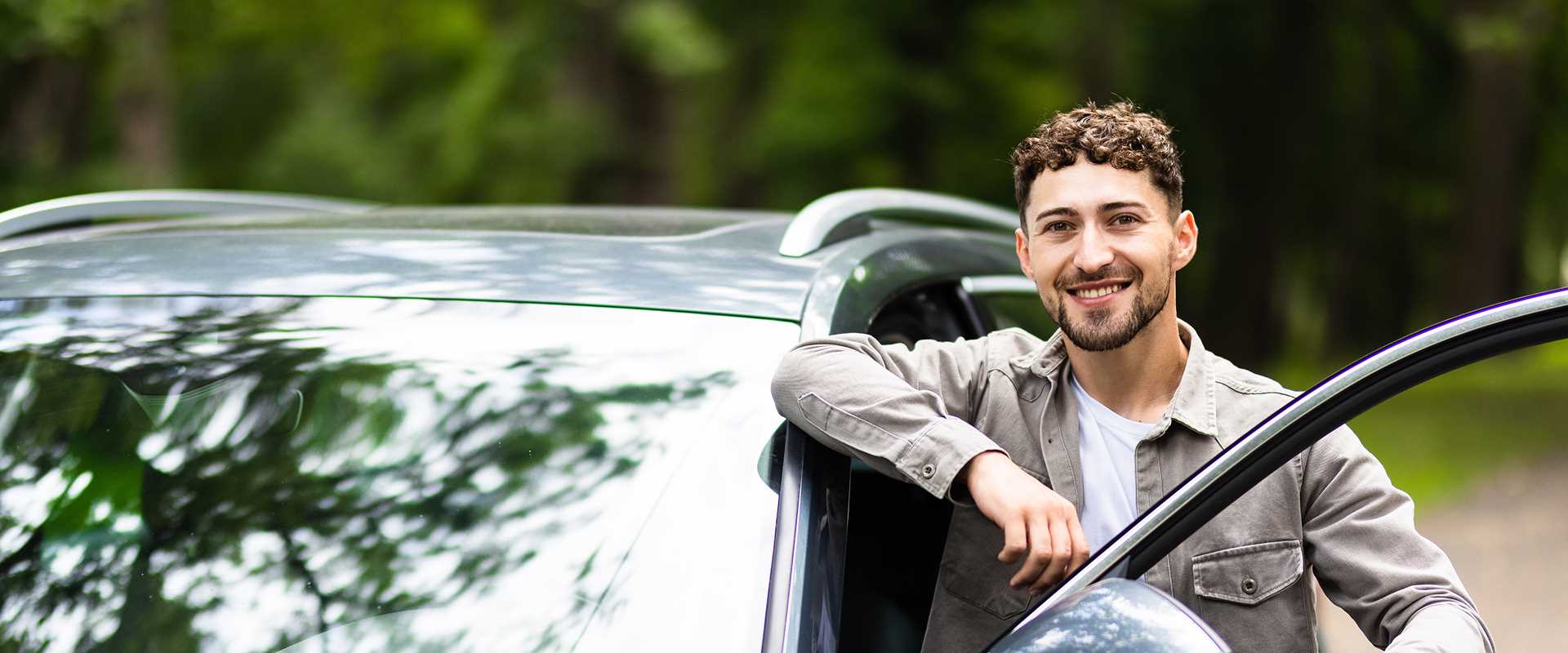 Homme souriant à côté de sa voiture de location sur le chemin du travail