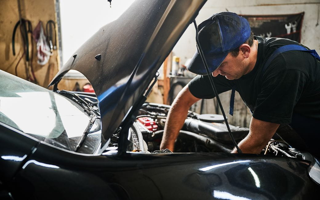 un réparateur portant une casquette, réparant un moteur de voiture.
