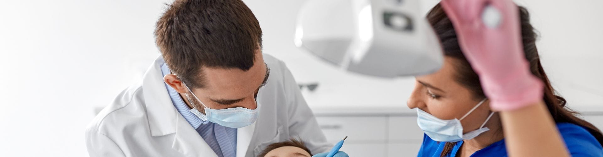 Un dentiste et son assistante portant un masque et des gants travaillent sur un patient