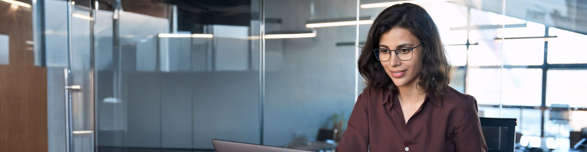 Une femme professionnelle portant des lunettes travaille sur un ordinateur portable dans un bureau moderne