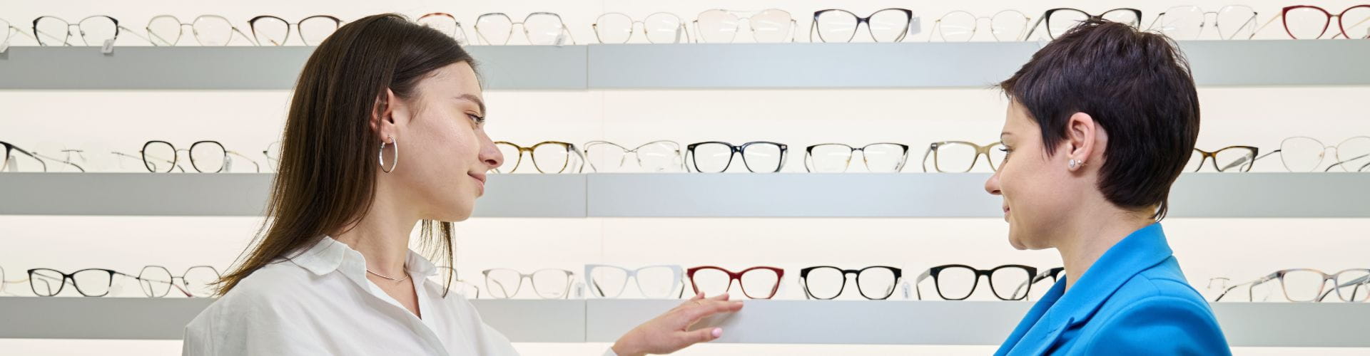 Deux femmes dans un magasin d'optique, l'une pointant des lunettes sur une étagère tandis que l'autre regarde