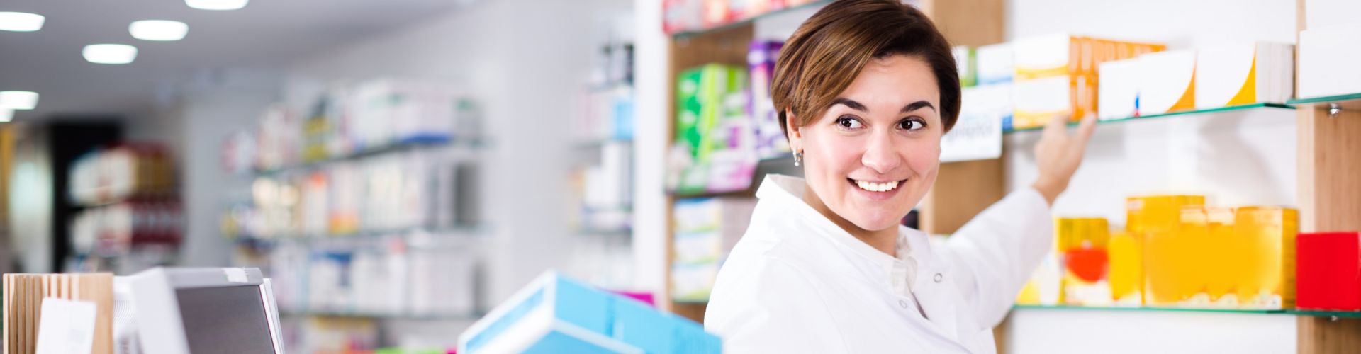 Une pharmacienne souriante cherche des produits sur une étagère