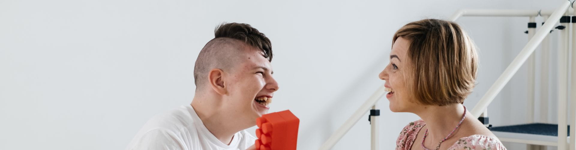 Un jeune homme réalise un exercice avec un bloc rouge avec l’aide d’une psychomotricienne