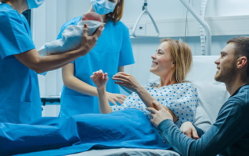Une soignante présente un nouveau-né à une mère souriante et à son partenaire dans une salle d'accouchement d'hôpital