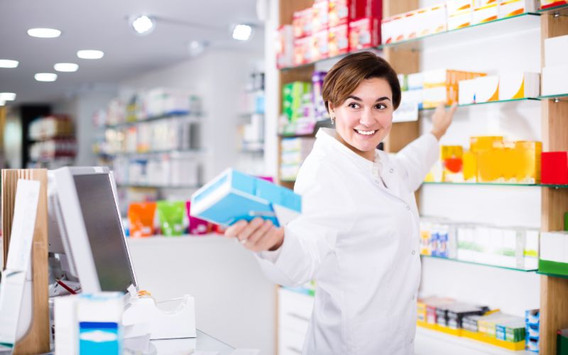 Une pharmacienne souriante cherche des produits sur une étagère