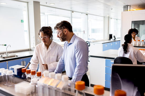 Deux scientifiques en blouses blanches et lunettes de protection travaillent dans un laboratoire avec un microscope et des éprouvettes