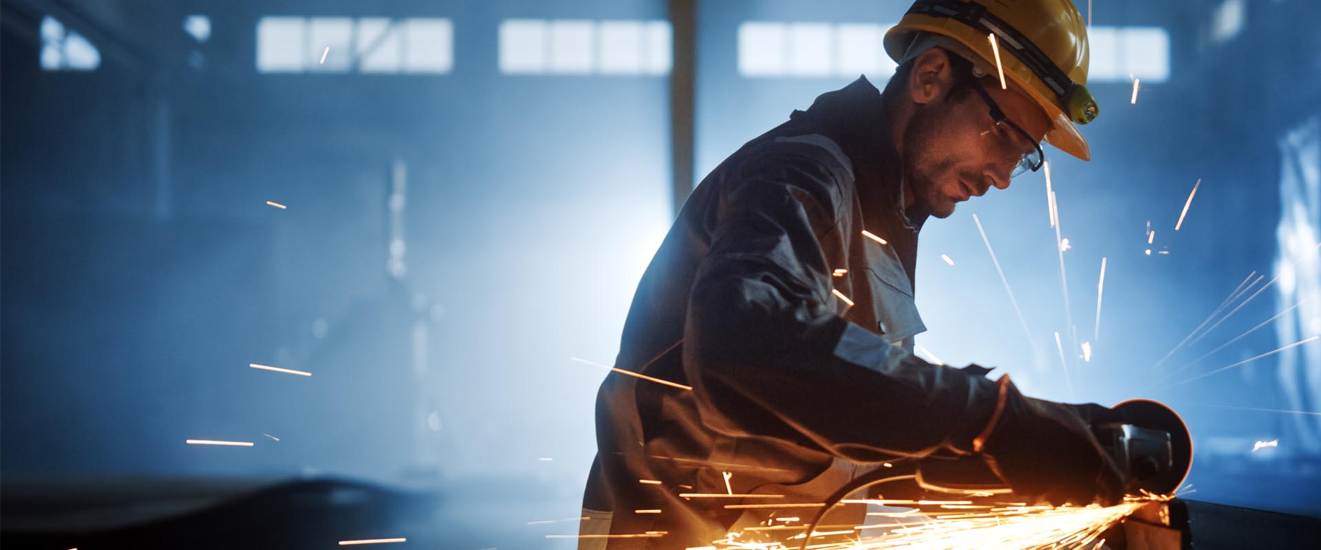 Industrial worker cutting metal with sparks in a factory setting