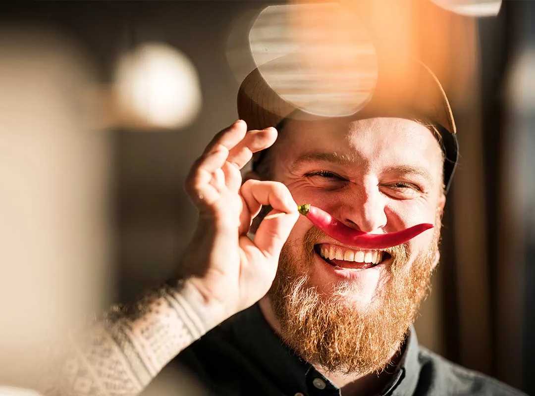 Een glimlachende medewerker die op speelse wijze een rood voorwerp voor één oog houdt in een creatieve werkruimte