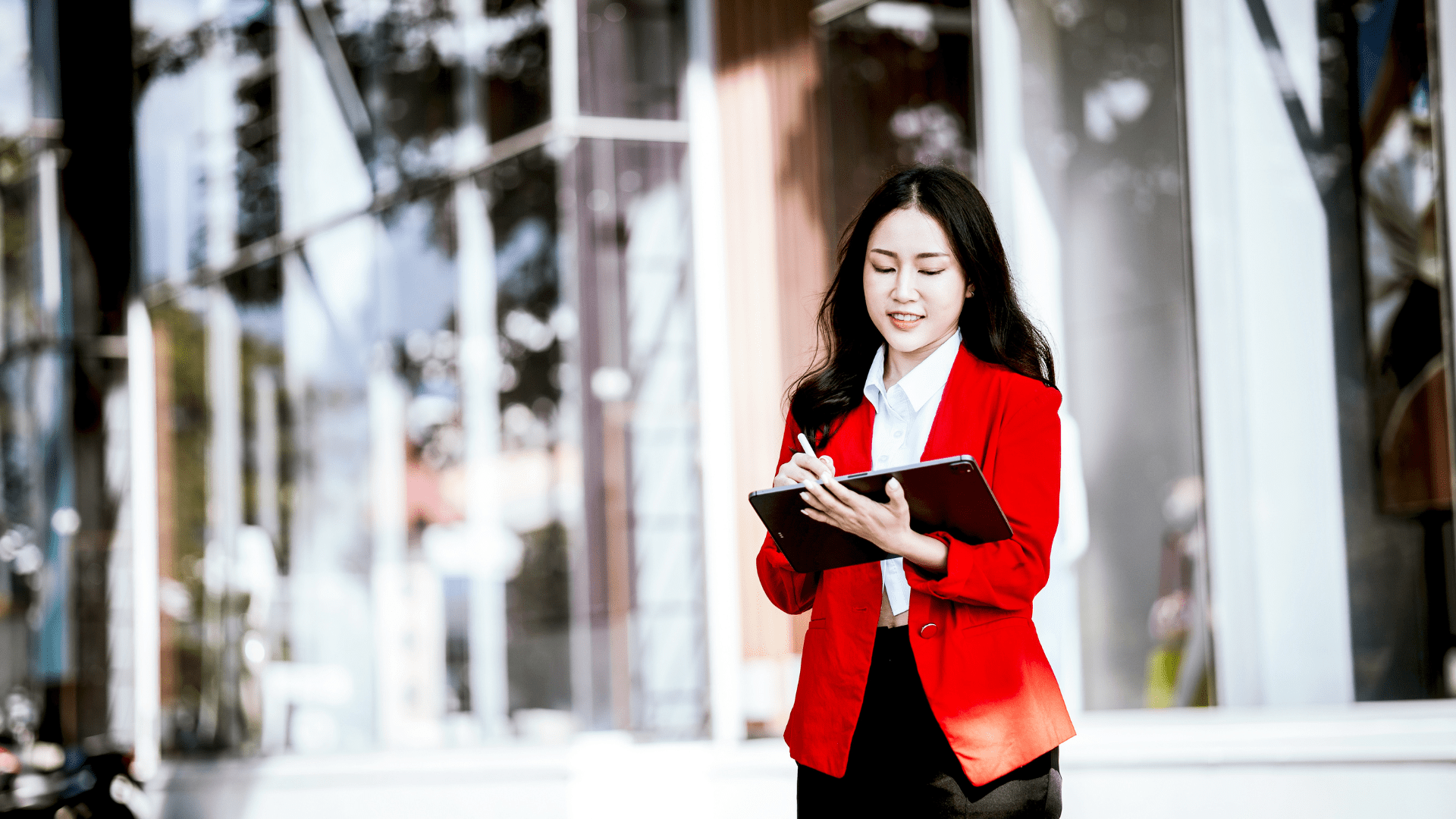 Femme portant un blazer rouge, debout dehors, écrivant dans son carnet