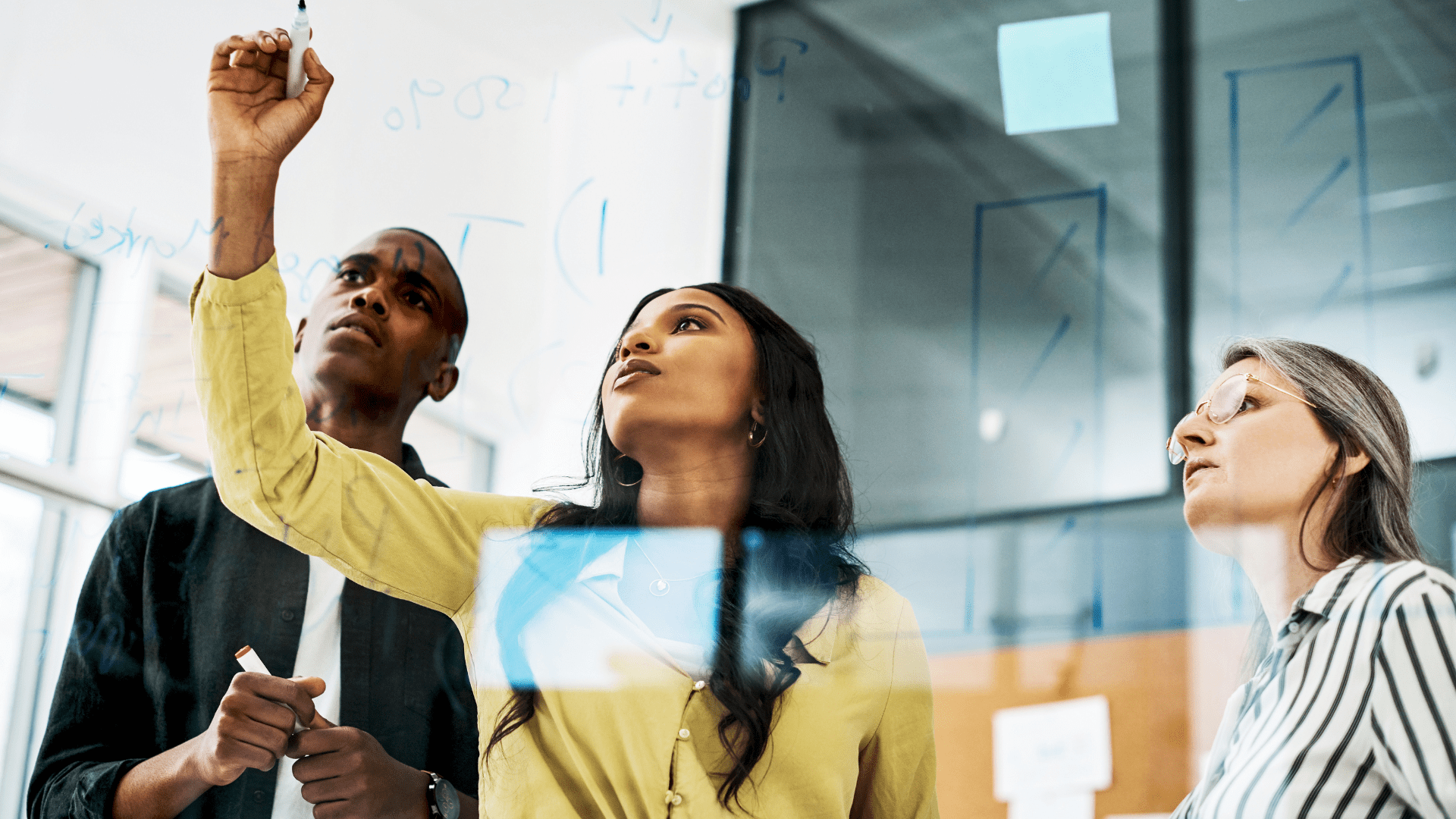 colleagues strategizing by writing on a white board in an office space