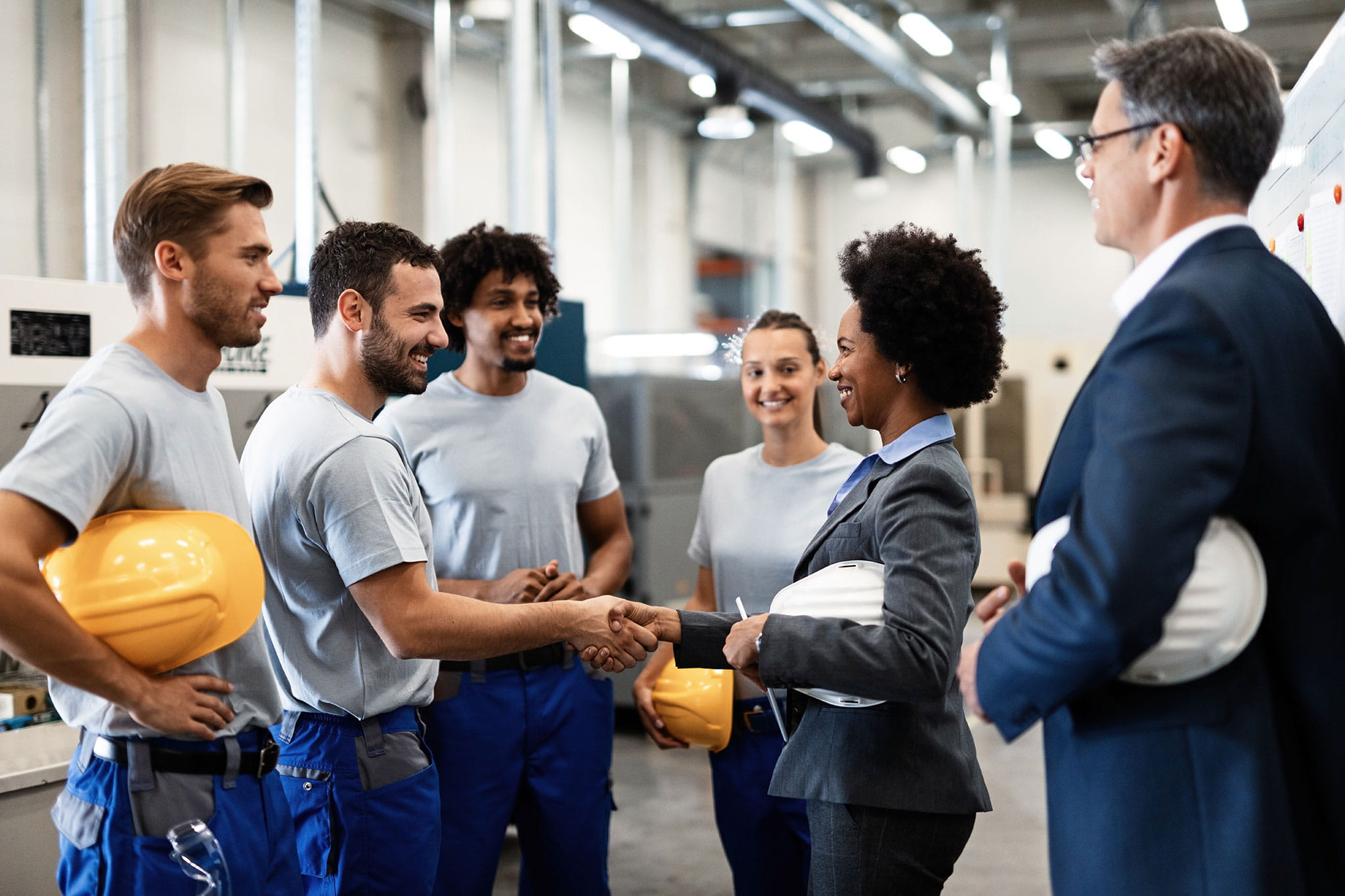 A team of Adecco associates wearing PPE having a stand-up meeting at the client's industrial worksite.
