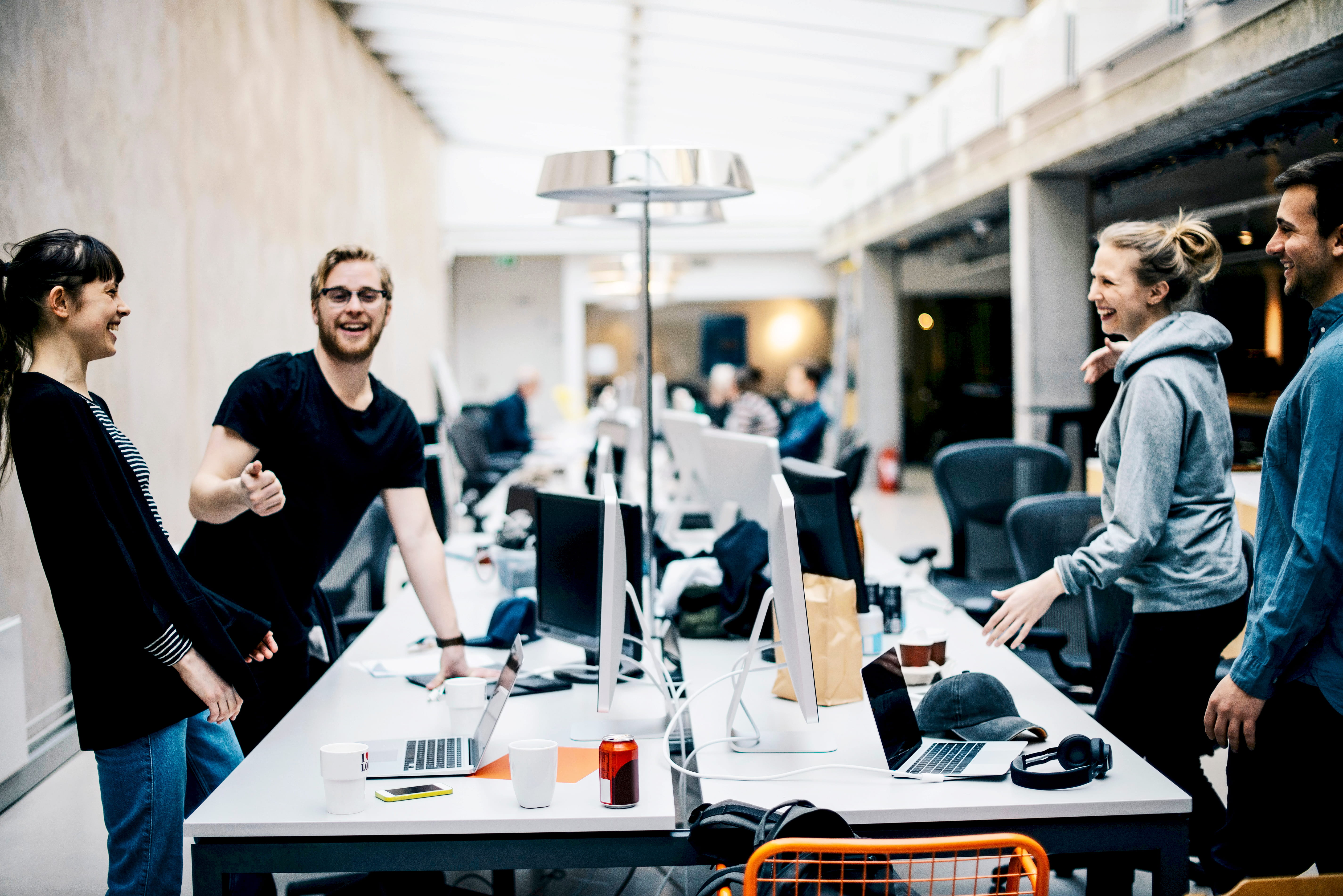 Des individus souriant et riant dans un environnement de travail qui semble être une salle de conférence, entourés d’écrans et d’ordinateurs.