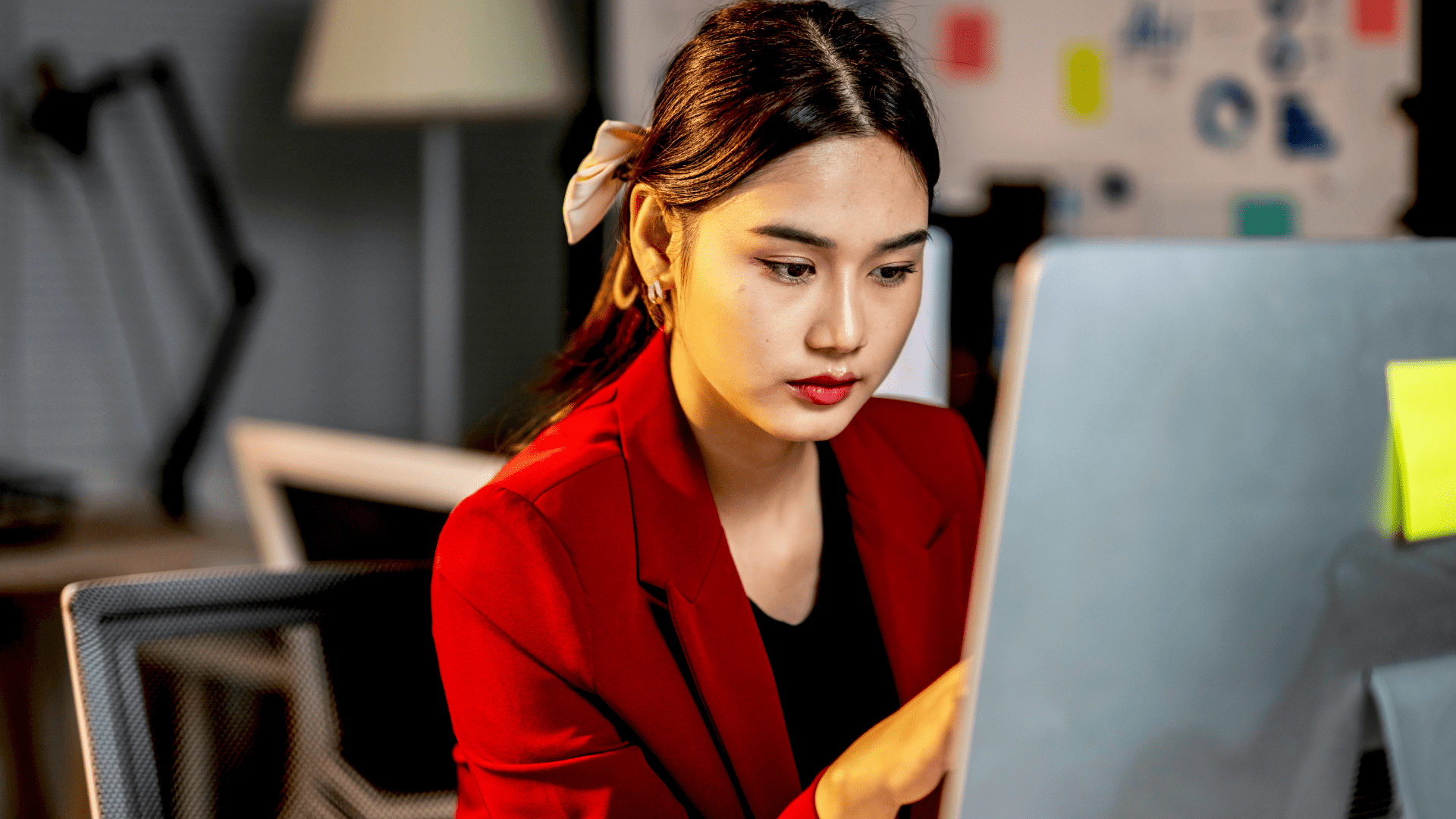 Une femme portant un veston rouge, concentrée sur l’écran de son ordinateur.