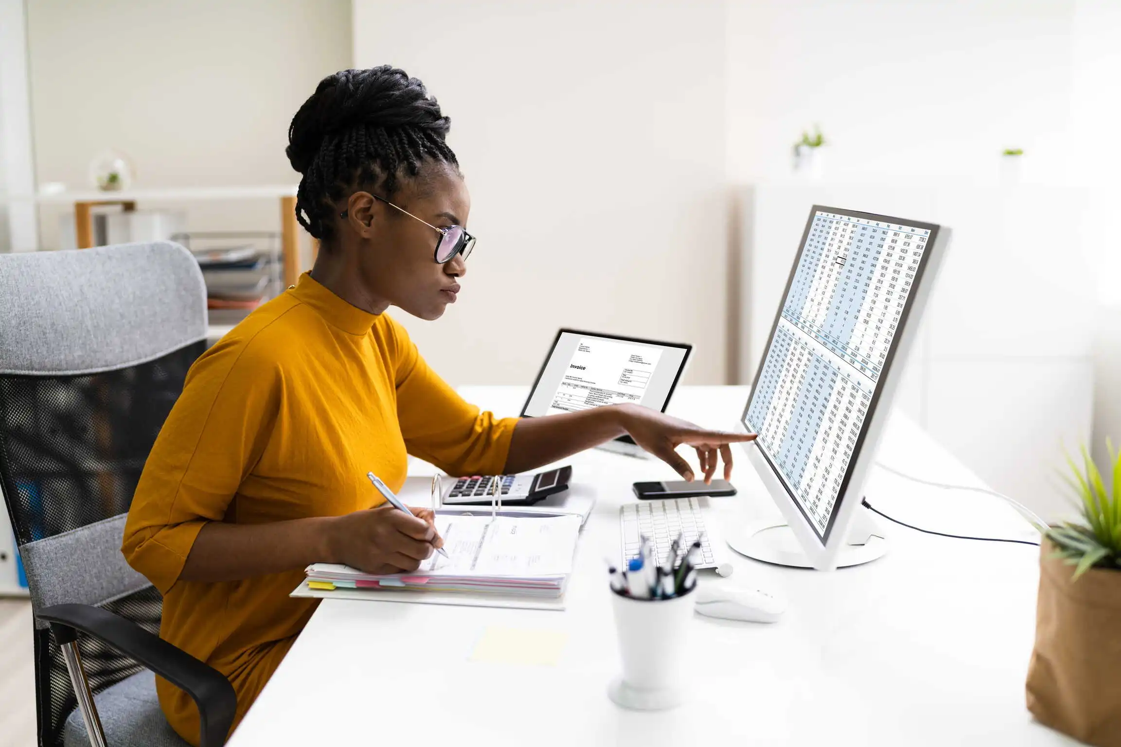 Une gestionnaire passe en revue le budget de son service et ses dépenses en ressources humaines en se référant à plusieurs écrans, à des dossiers et à une calculatrice sur son bureau. Une gestionnaire passe en revue le budget de son service et ses dépenses en ressources humaines en se référant à plusieurs écrans, à des dossiers et à une calculatrice sur son bureau.