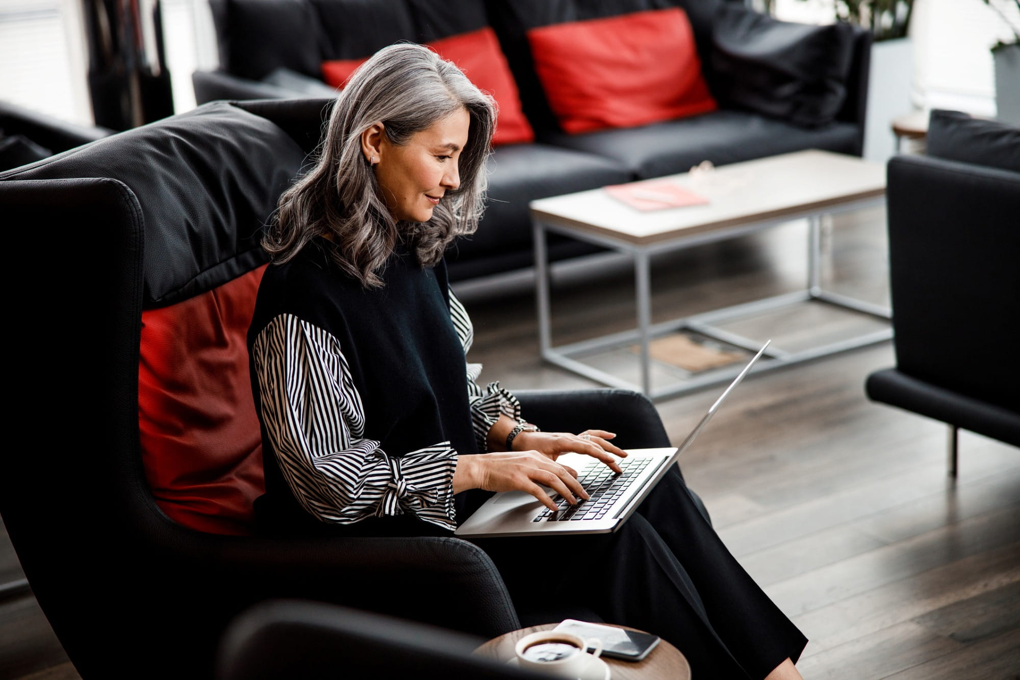 Une femme d'affaires assise dans un fauteuil dans son bureau, travaillant sur un ordinateur portable moderne Une femme d'affaires assise dans un fauteuil dans son bureau, travaillant sur un ordinateur portable moderne