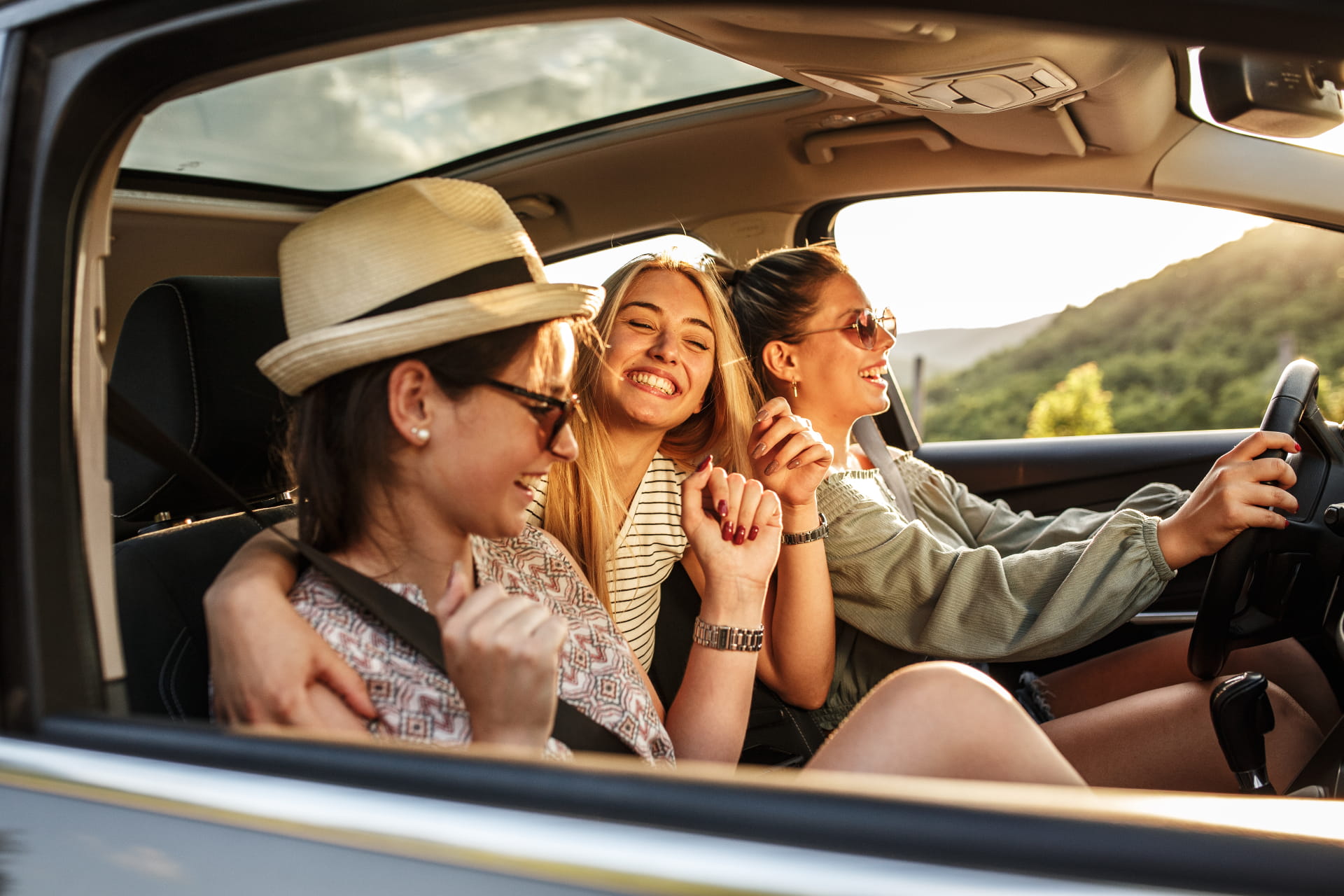 Drei Frauen sitzen im Auto. Die Sonne scheint.