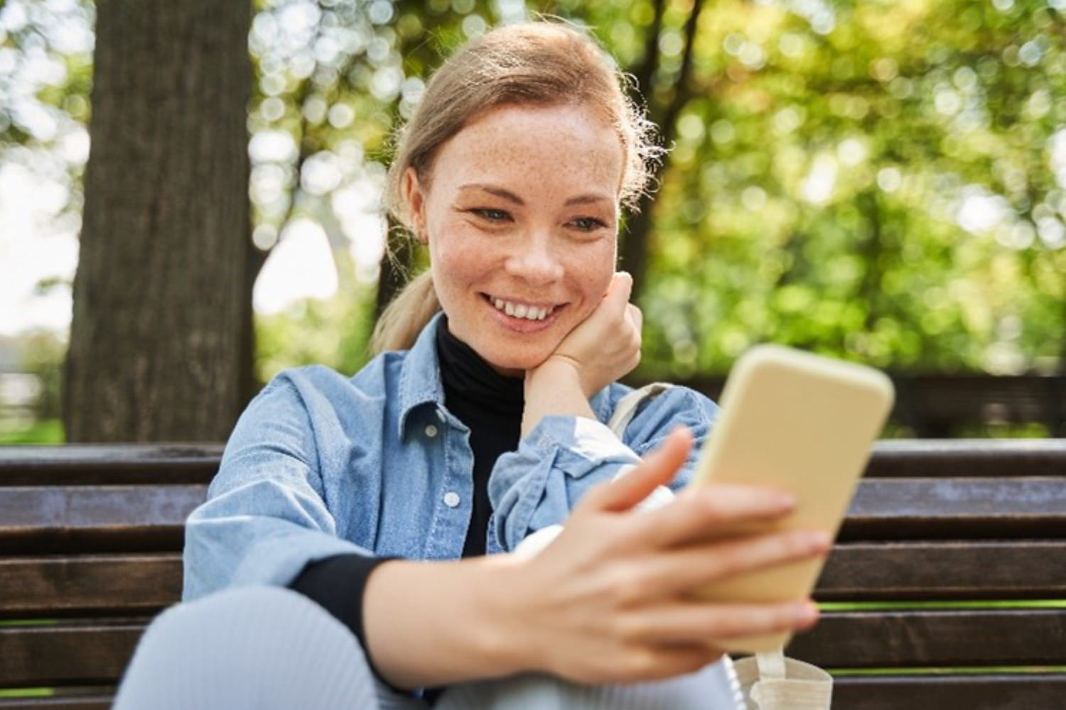 Frau sitzt mit Smartphone auf einer Bank.