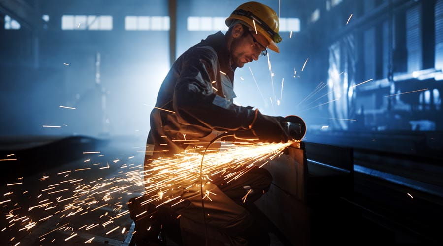Industrial worker cutting metal with a grinding tool, sparks flying