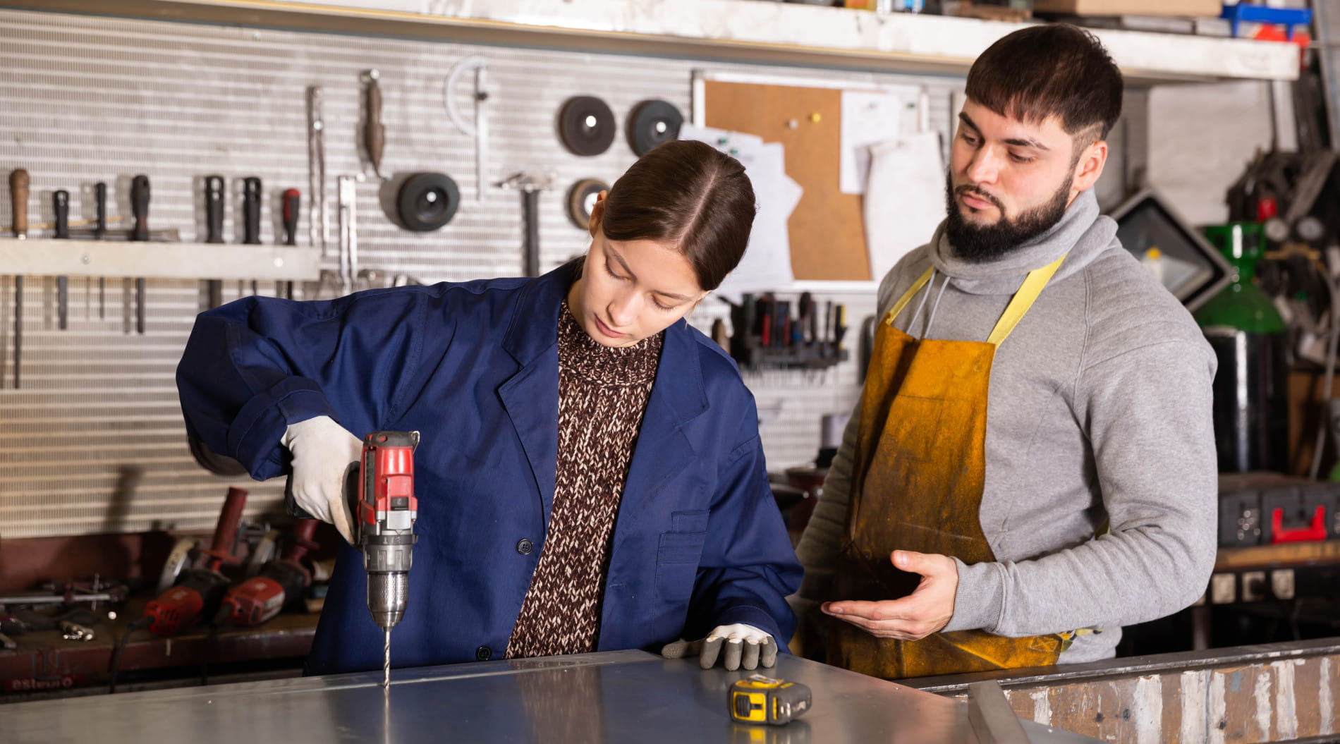 Mentor guiding student with power drill in workshop