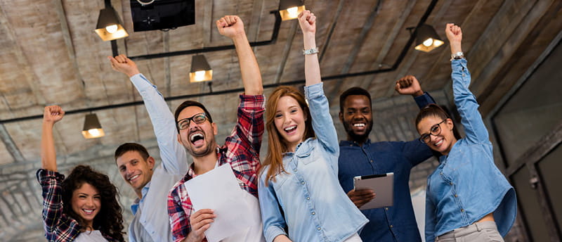Group of six people in a modern office raising their arms in celebration.