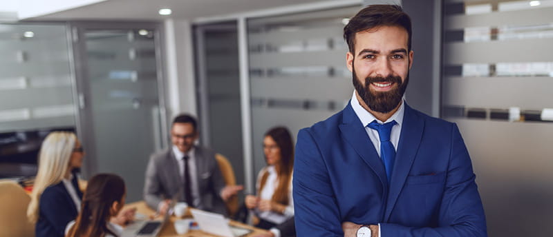 Person in a blue suit standing confidently in front of a team working together in a modern office