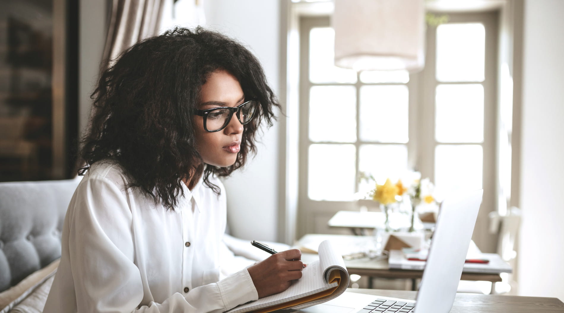 Person writing at desk with laptop, updating CV