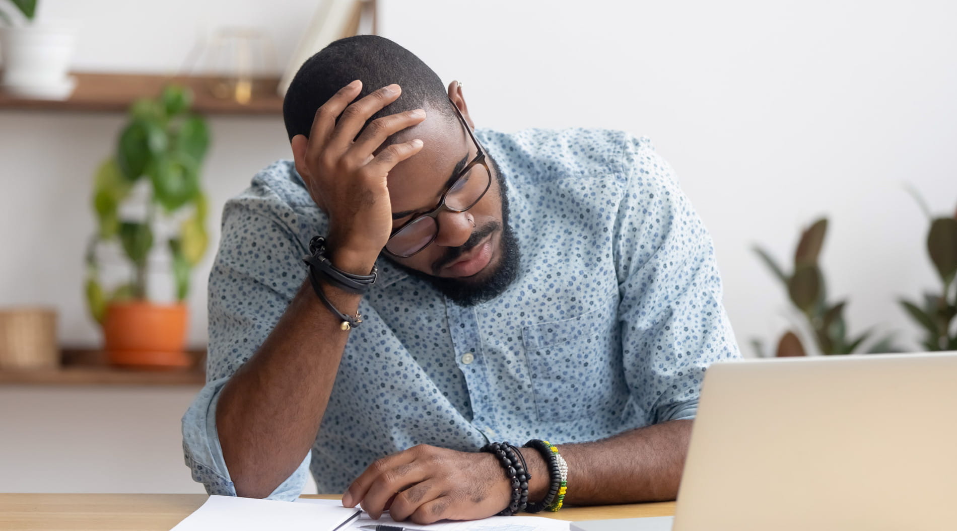 Person at desk with laptop, hand on head, appearing stressed